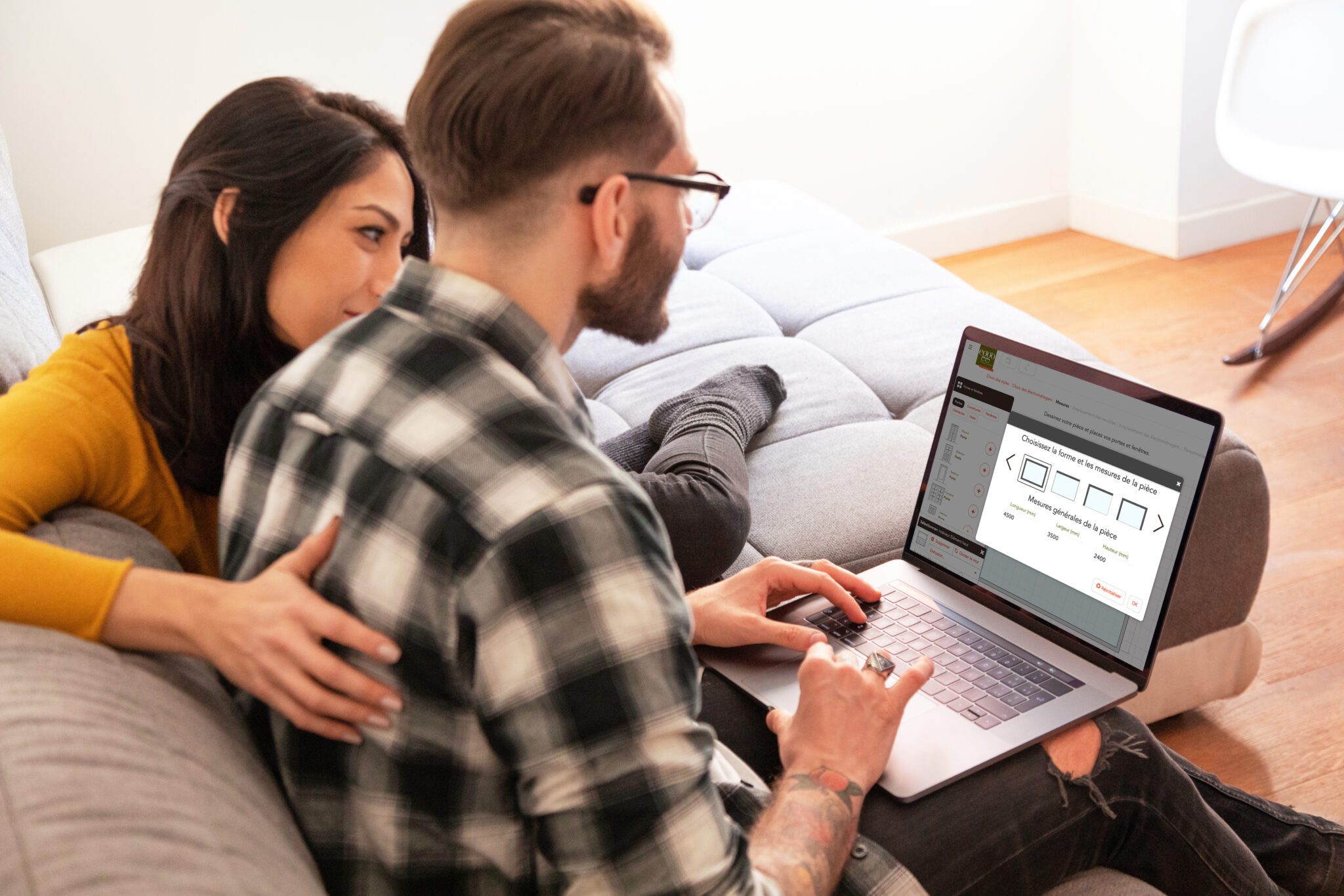 Un couple assis sur un canapé consulte un configurateur de pièces sur un ordinateur portable.