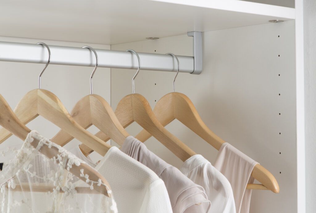 Des cintres en bois suspendus dans une penderie blanche contiennent des vêtements de couleur claire, dont un en dentelle.