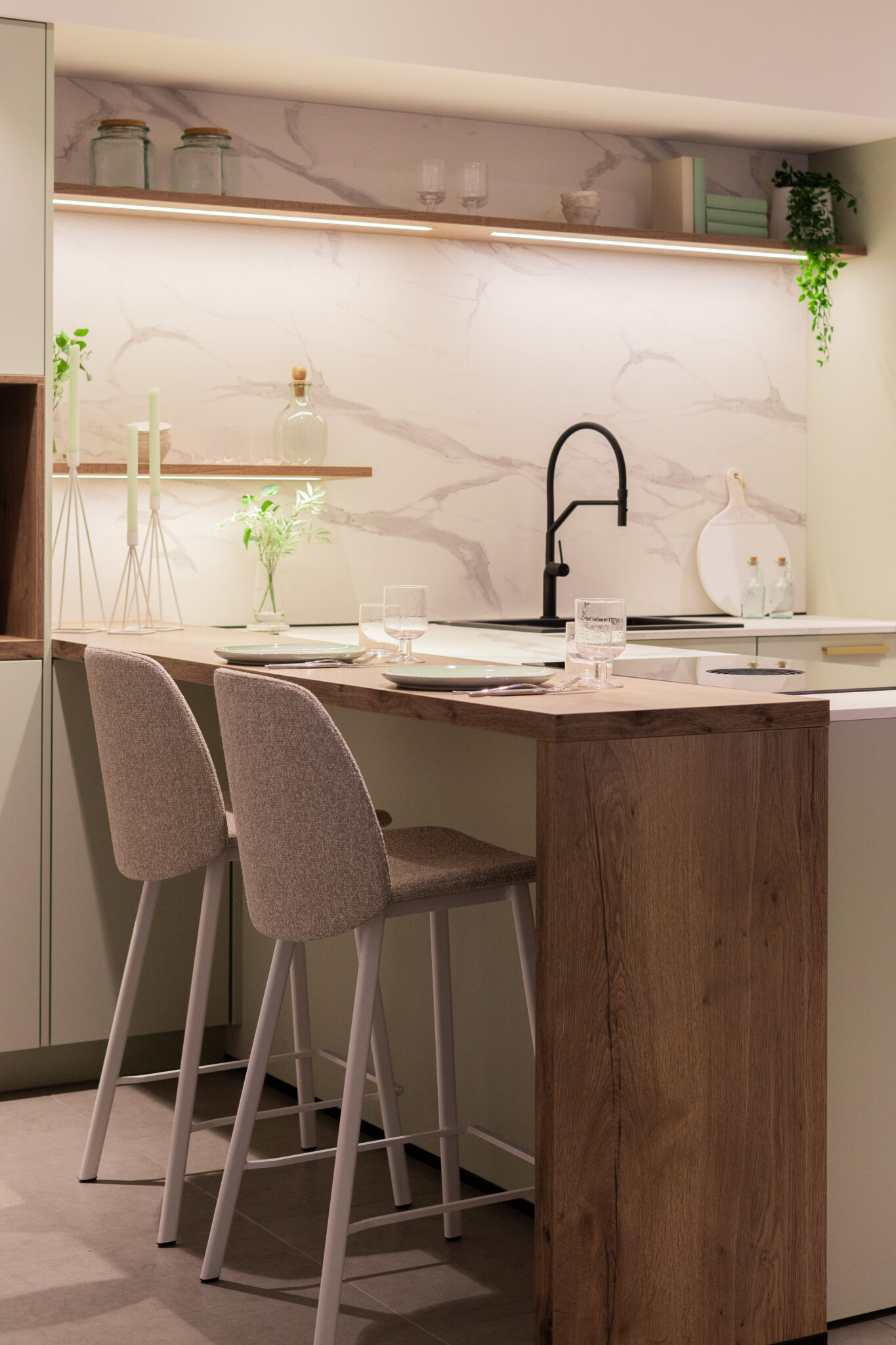 Deux chaises rembourrées grises sont placées devant un îlot en bois clair dans une cuisine moderne avec un robinet noir.