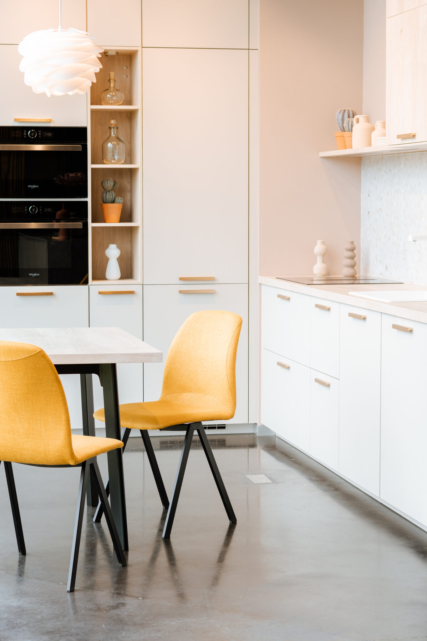 Cuisine moderne avec meubles blancs, chaises jaunes autour d'une table et décorations sur étagères intégrées.