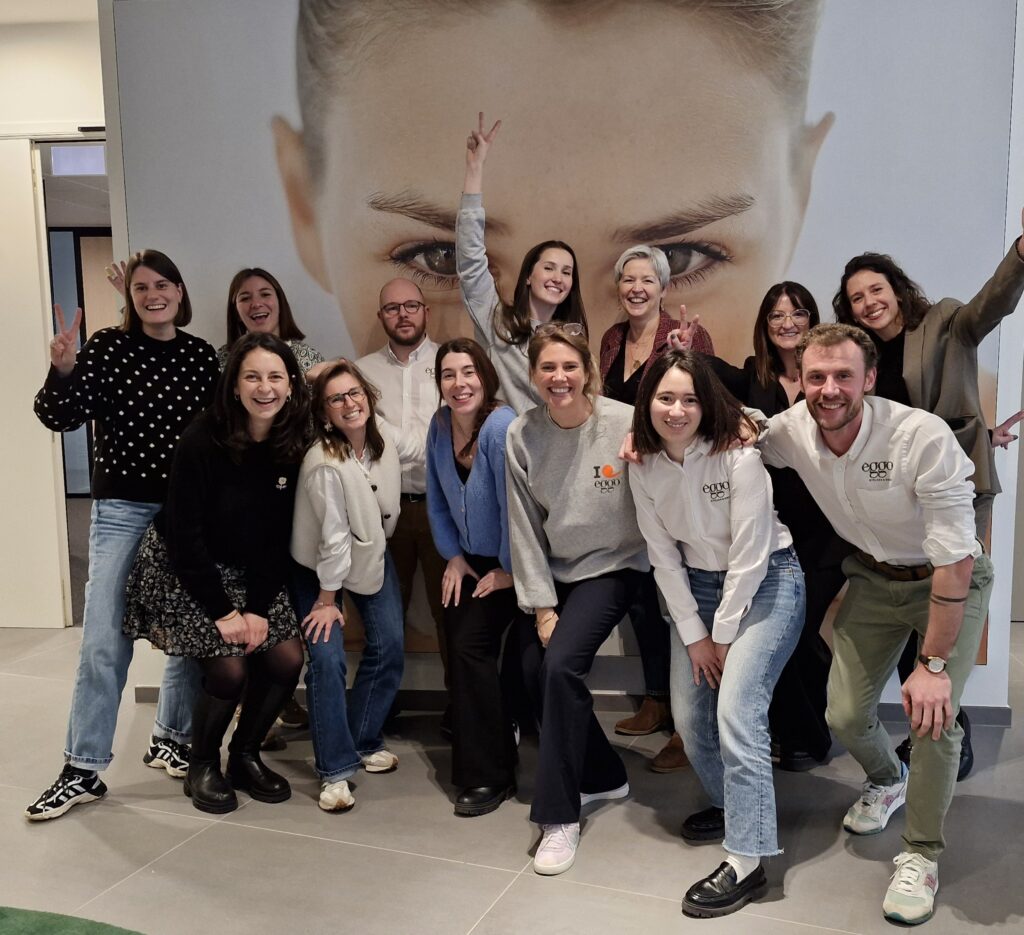 Un groupe de personnes souriantes pose devant une grande affiche murale avec un visage, habillées de manière décontractée.