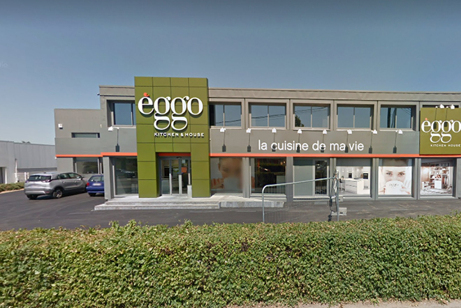 Façade d'un magasin èggo avec une enseigne verte et blanche, entourée de fenêtres et d'un parking avec des voitures garées.