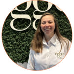 Une femme en chemise blanche avec le logo èggo se tient devant un mur végétal avec le texte èggo en lettres blanches.